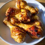 A plate of golden-brown, juicy Lemon Pepper Air Fryer Drumsticks, seasoned with herbs and spices.