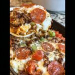 A scoop of cheesy Low-Carb Pizza Casserole with pepperoni, sausage, and vegetables being lifted.