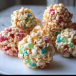 Close-up of several No-Bake Marshmallow Popcorn Balls mixed with colorful gumdrops, resting on a white plate.