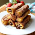 Stack of golden Nutella-Filled French Toast Rollups coated in cinnamon sugar, with melted chocolate oozing out.