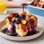 A slice of Overnight Blueberry French Toast Bake being drizzled with blueberry syrup.