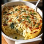 A close-up of a baked spaghetti squash filled with creamy Alfredo sauce and spinach, topped with melted cheese and herbs.