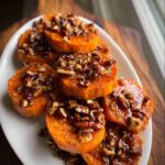 A stack of bright orange Sweet Potato Rounds with Pecan Maple Topping glistening on a white platter.