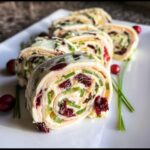 Close-up of sliced Turkey & Cranberry Pinwheels filled with cream cheese, chives, and dried cranberries on a white platter.