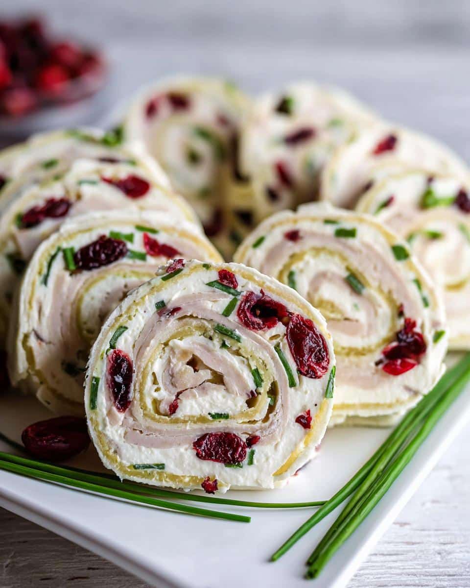Close-up of sliced Turkey & Cranberry Pinwheels featuring cream cheese, turkey, dried cranberries, and chives.