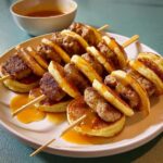 Skewers of Turkey Sausage Pancake Minis drizzled with syrup on a white plate.