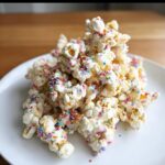A mound of white chocolate-coated Unicorn Sprinkle Popcorn generously topped with colorful rainbow sprinkles.