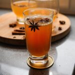 A tall glass of Vanilla Chai Apple Cider Mocktail garnished with star anise and cinnamon sticks.