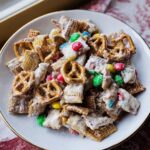 A white chocolate coated Christmas Chex Mix featuring pretzels, cereal, and colorful holiday candies.