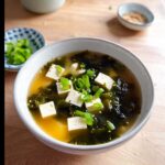 A bowl of 10-Minute Classic Miso Soup featuring cubes of tofu, dark seaweed, and topped with sliced green onions and sesame seeds.