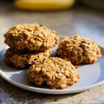 Four golden brown 2-Ingredient Banana Oat Cookies stacked and placed on a light gray plate.
