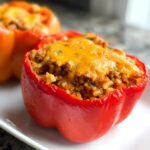 A close-up of a bright red bell pepper filled with taco meat and rice, topped with melted cheddar cheese, part of the 30-Minute Taco Stuffed Peppers.