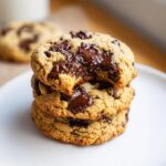 A stack of three gooey Almond Flour Chocolate Chip Cookies with melted chocolate chunks and a bite taken out of the top one.