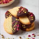 Stack of Almond Flour Shortbread cookies dipped in dark chocolate and topped with pistachios and rose petals.