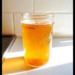 A bright, golden Apple Cider Vinegar Detox Drink served in a clear Ball mason jar, topped with spices.