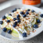 A plate of Apple Nachos with Greek Yogurt Drizzle, topped with fresh blueberries and sliced almonds.