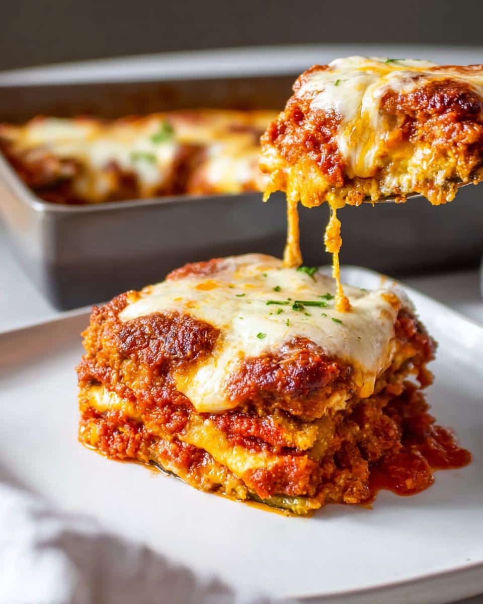 A gooey, cheesy serving of Baked Eggplant Parmesan being lifted from a baking dish.