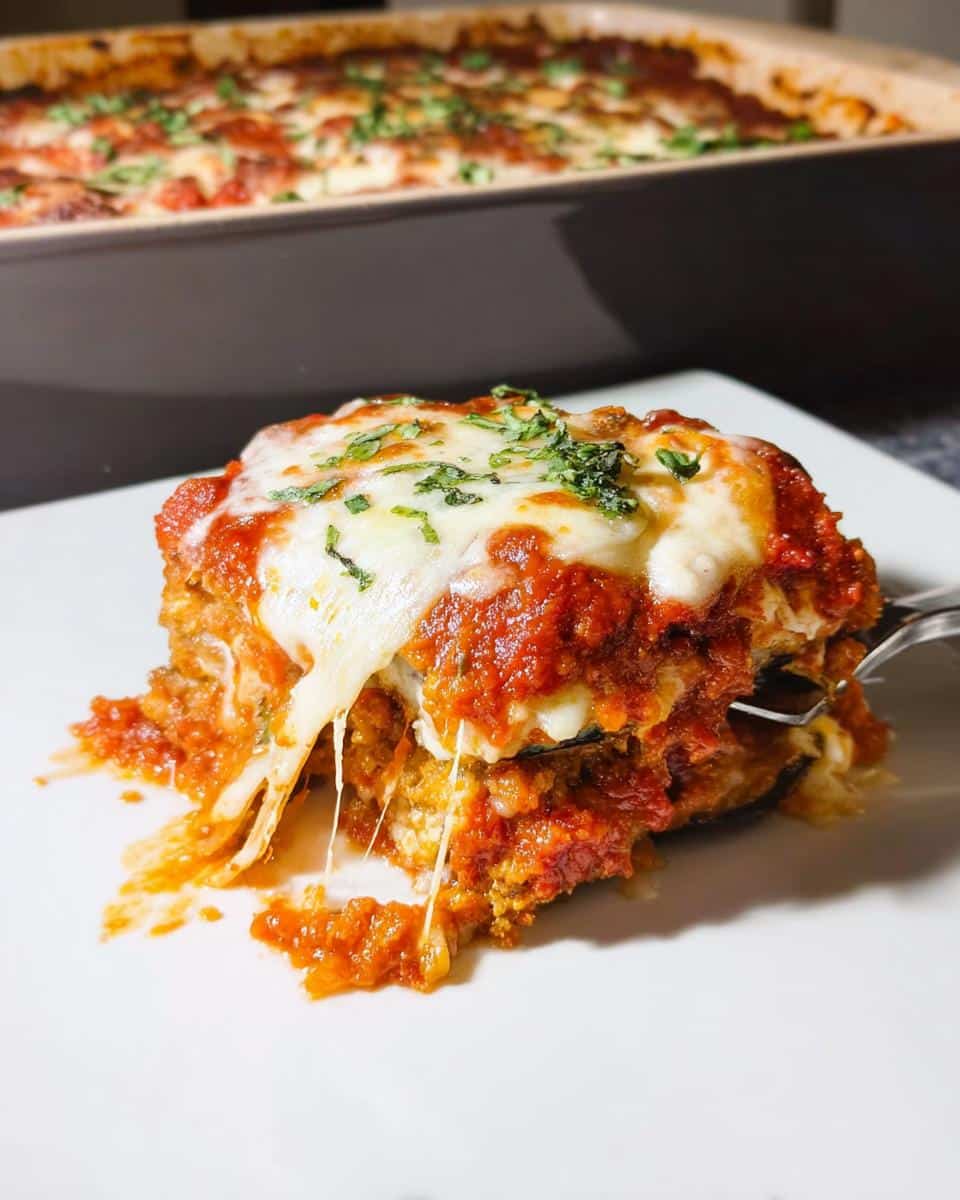 A close-up of a serving of Baked Eggplant Parmesan covered in melted mozzarella and tomato sauce, showing a cheese pull.