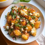 Close-up of golden roasted Baked Feta Potatoes with Garlic & Herbs, topped with crumbled feta and fresh basil.