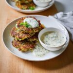 Stack of golden brown Baked Zucchini Fritters with a dollop of yogurt dip and mint garnish.