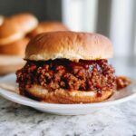 A close-up of a fully assembled BBQ Beef Sloppy Joes sandwich piled high with saucy ground beef on a toasted bun.