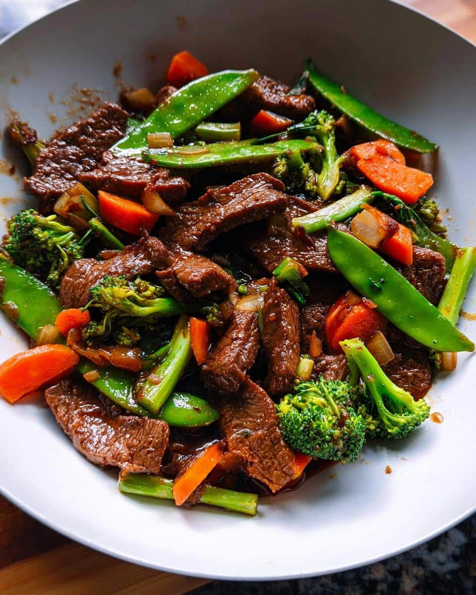 Close-up of tender beef slices mixed with bright green snow peas, broccoli, and carrots in a rich soy-garlic sauce, serving as a Beef & Veggie Stir-Fry.