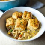 A white bowl filled with creamy chicken pot pie filling topped with five golden brown biscuits, a perfect Biscuit-Topped Crockpot Chicken Pot Pie.