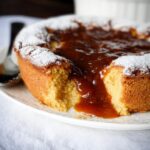 Close-up of a warm Butterscotch Self-Saucing Pudding Thermomix dessert with gooey sauce oozing out, dusted with powdered sugar.