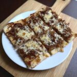 Six rectangular slices of Caramelized Onion & Gruyère Flatbread topped with melted cheese, served on a white plate.