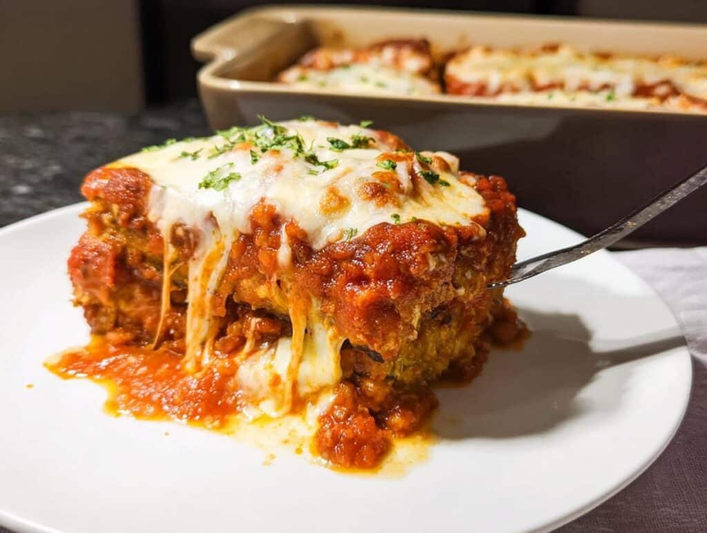 A gooey, cheesy slice of Baked Eggplant Parmesan being lifted with a fork, covered in marinara sauce.