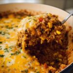 A spoonful of cheesy Mexican Beef Rice Casserole being lifted from the pan, showing melted cheese and corn.
