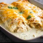 Close-up of Cheesy Sour Cream Chicken Enchiladas covered in melted white and cheddar cheese sauce.