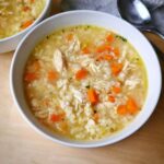 Close-up of a white bowl filled with hearty Chicken Lemon Rice Soup, featuring shredded chicken, rice, and bright orange carrots.