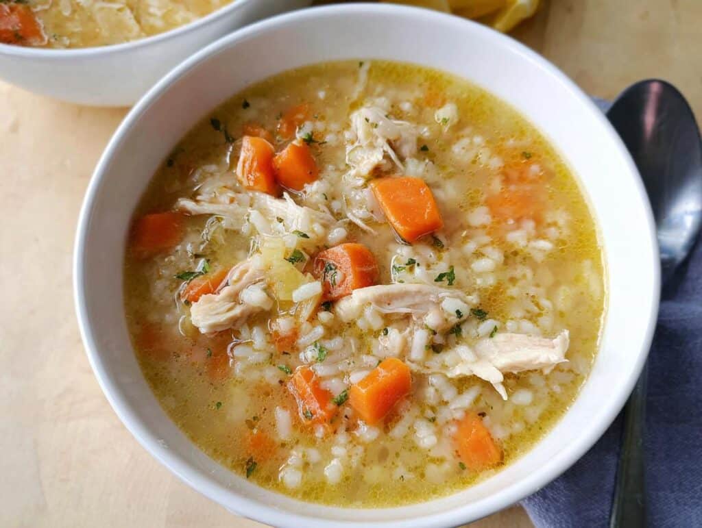 Close-up of a white bowl filled with rich Chicken Lemon Rice Soup, featuring shredded chicken, rice, and bright orange carrots.