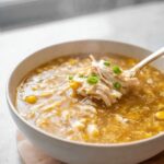 A spoonful of shredded chicken and corn being lifted from a bowl of hot Chicken & Sweet Corn Soup.
