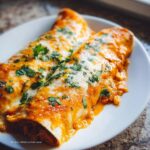 Two cheesy Chipotle Chicken Enchiladas with Corn, smothered in sauce and topped with fresh cilantro.