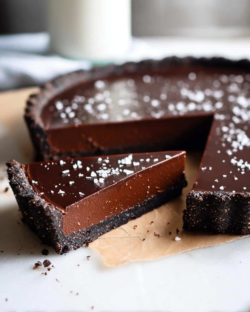 A slice of rich Chocolate Ganache Tart with a dark crust, topped with flaky sea salt.