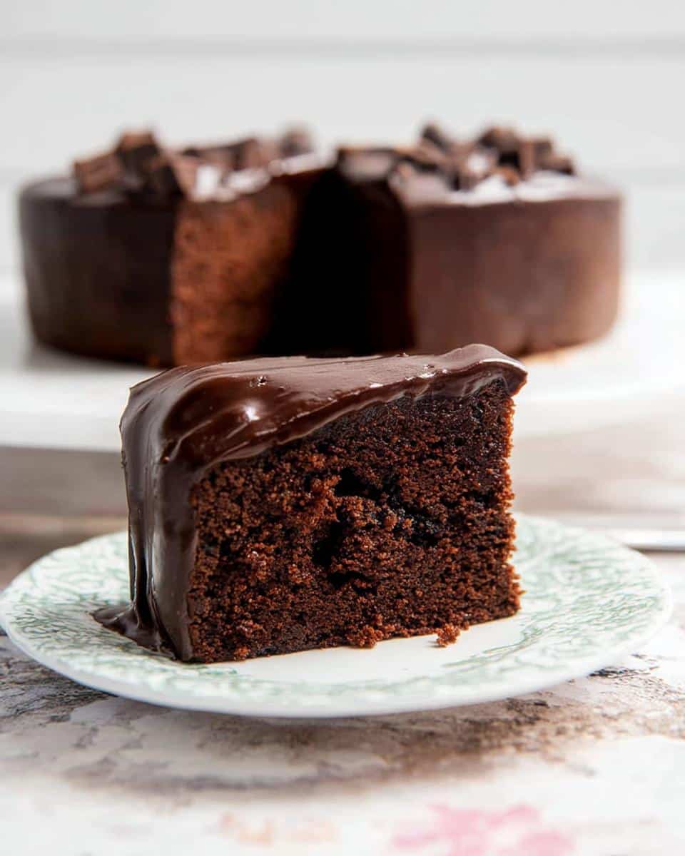 A close-up of a moist slice of Chocolate Mud Thermomix Cake with glossy dark chocolate ganache.
