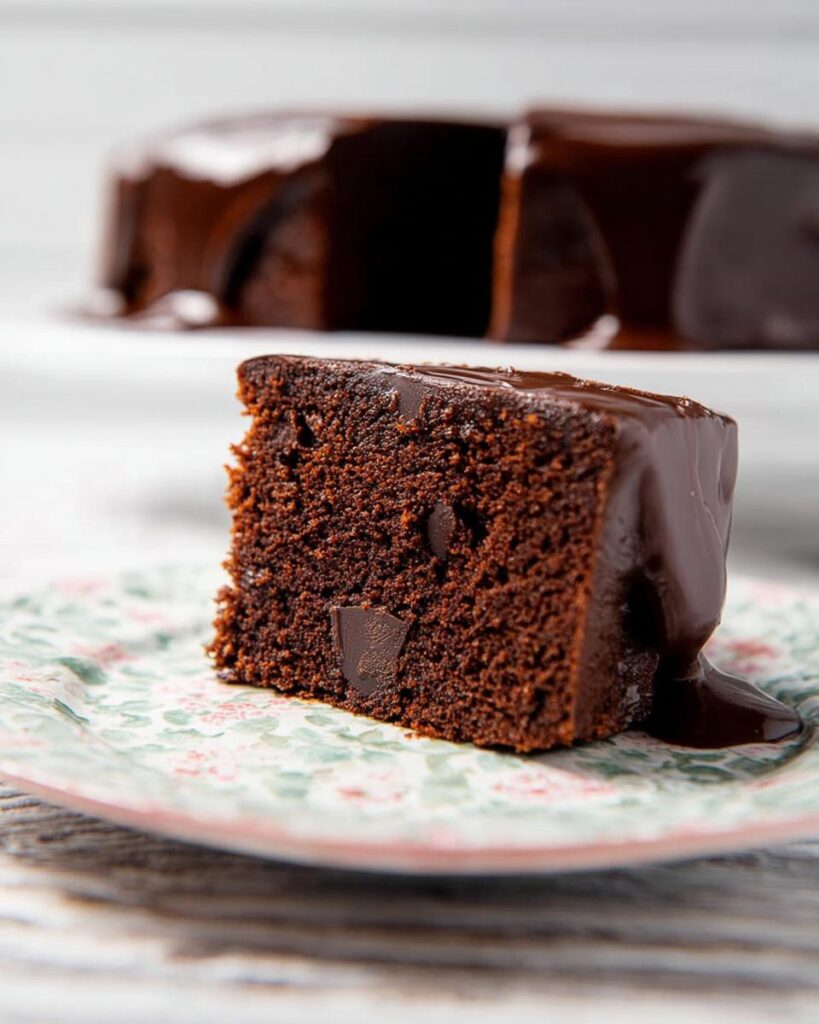 A close-up of a moist slice of Chocolate Mud Thermomix Cake topped with glossy chocolate ganache.