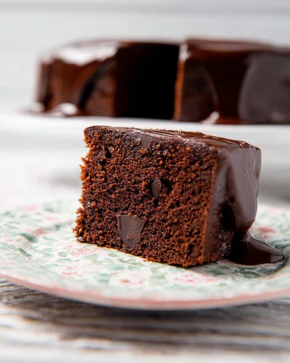 A close-up of a moist slice of Chocolate Mud Thermomix Cake topped with glossy chocolate ganache.