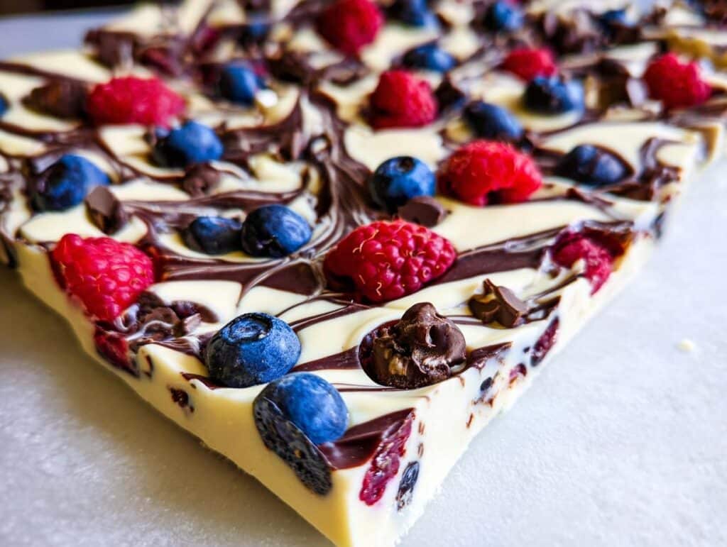 A close-up view of a piece of white and dark swirled Chocolate Yogurt Bark with Berries, topped with fresh raspberries and blueberries.