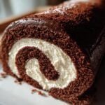A close-up cross-section of a rich Chocolate Yule Log showing the dark chocolate cake rolled around a thick white cream filling.