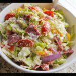 A white bowl filled with a creamy Chopped Italian Grinder Bowl salad featuring lettuce, salami, tomatoes, and red onion.