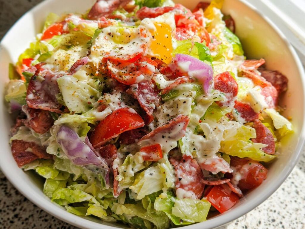 Close-up of a Chopped Italian Grinder Bowl featuring chopped lettuce, tomatoes, red onion, salami, and creamy dressing.