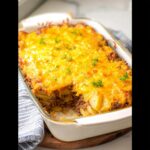 A baked Classic Beef & Potato Casserole in a white dish with a thick layer of melted cheddar cheese on top.