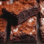 Close-up of rich, dark Classic Fudgy Thermomix Brownies stacked, showing their cracked, shiny tops.