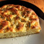 Close-up of a golden-brown slice of Classic Gluten-Free Focaccia Bread topped with rosemary and coarse sea salt.