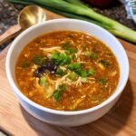 A white bowl filled with steaming Classic Hot & Sour Chicken Soup, garnished with green onions.
