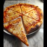 A whole Classic New York-Style Cheese Pizza, sliced into wedges and served on a white plate.