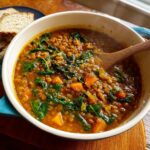 Close-up of steaming Classic Vegan Lentil Soup with chunks of sweet potato and wilted spinach.